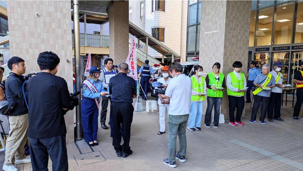きりしま国分山形屋前で、一日警察署長が来場者に啓発資料を手渡し、蛍光ベスト姿の学生らが活動に参加する様子