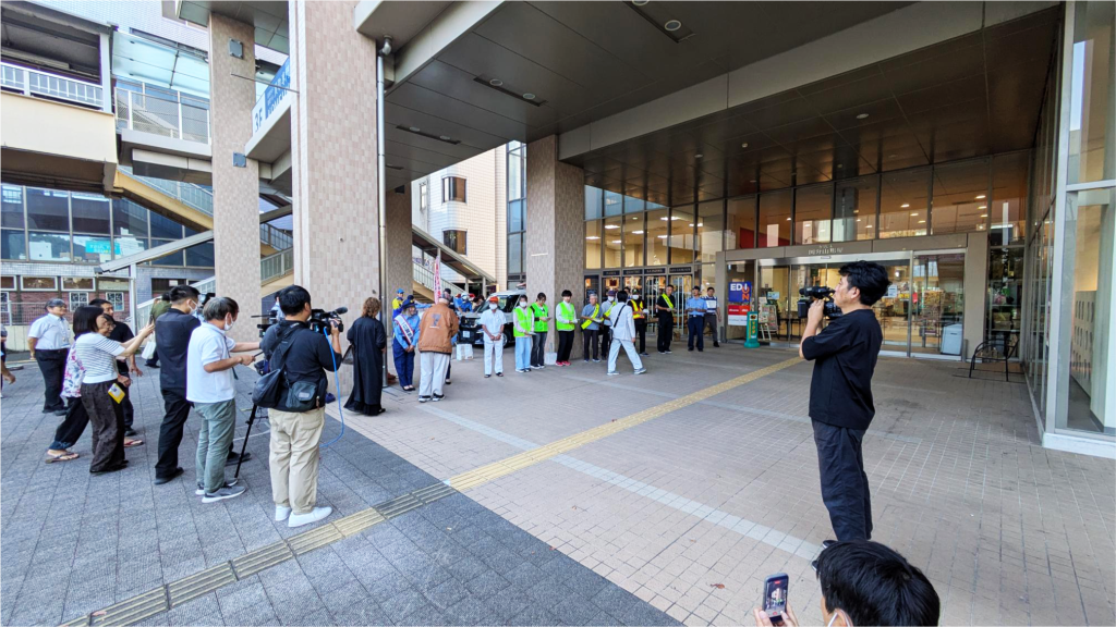 きりしま国分山形屋の入口前に学生や警察関係者らが並び、防犯啓発活動の様子を報道陣が撮影する会場全景