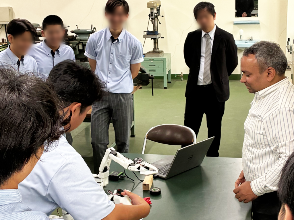 ロボットアームの操作体験をする生徒と、その様子を見守る教員や他の生徒たち